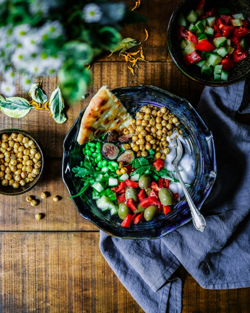 A bowl of food with vegetables, chickpeas, herbs and wholesome bread.