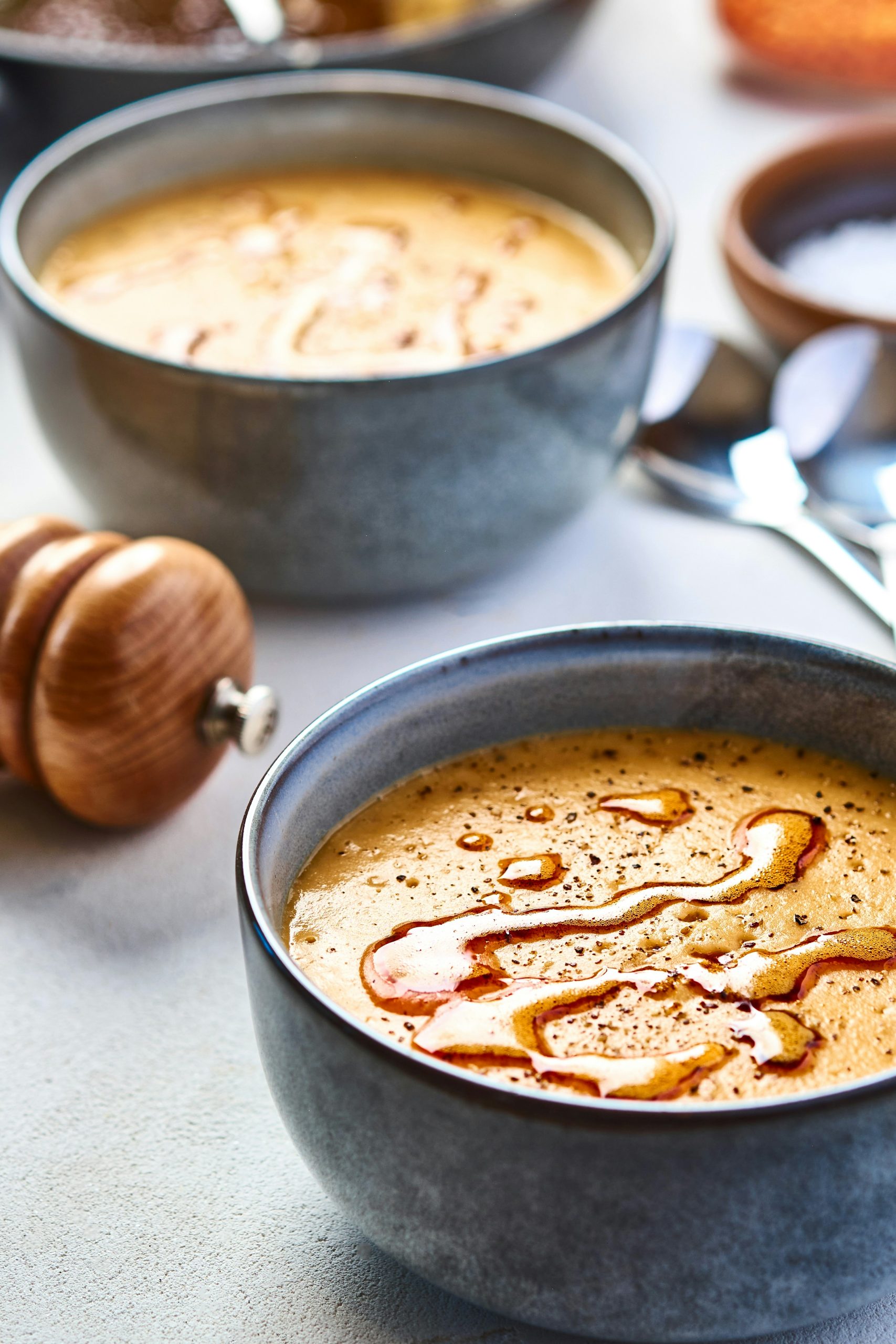 red lentil dhal in a bowl with oil drizzled over the top, served on a table next to a pepper mill and a spoon